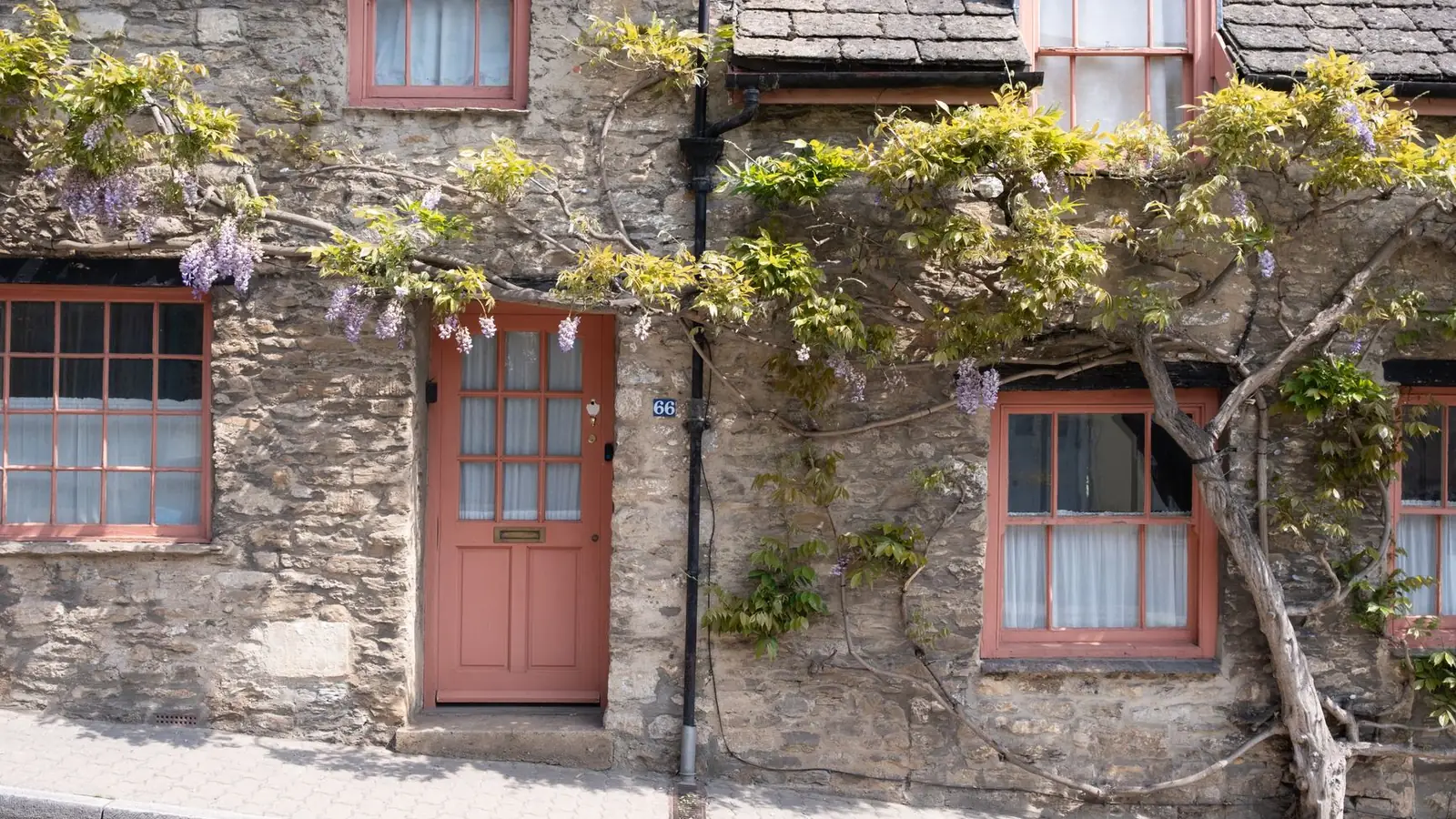 A coral painted front door in a stone cottage, framed by climbing wisteria.
