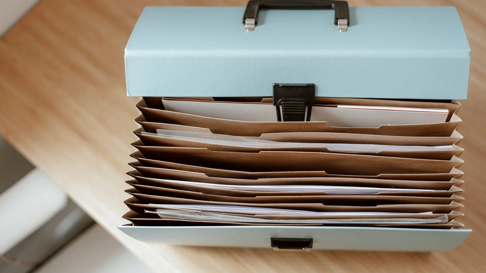 From above of briefcase for documents with papers placed on wooden table in daytime